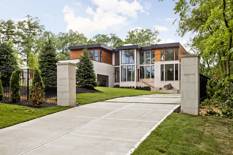 Contemporary custom home with cedar and limestone facade behind a gated driveway lined with evergreens