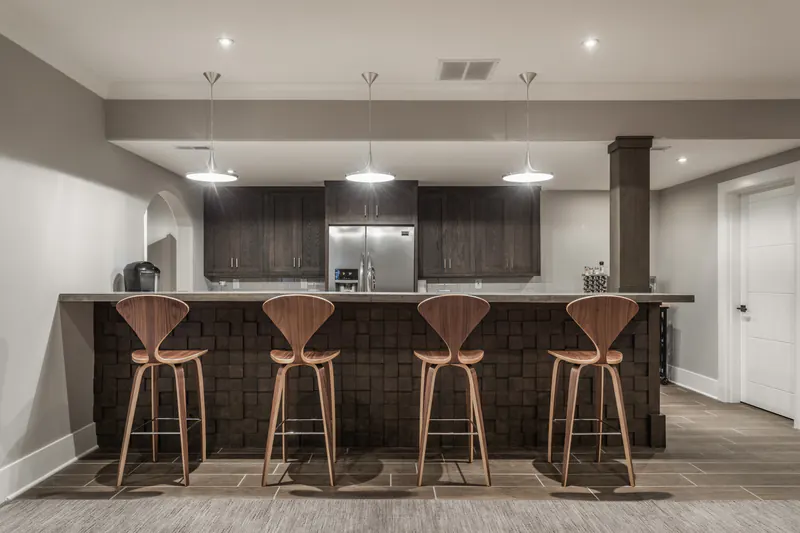 Custom bar and kitchenette with dark wood cabinetry, pendant lights and molded walnut bar stools