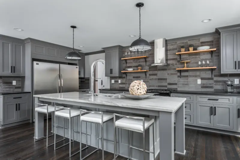 Gray shaker-style kitchen with a marble island, open wood shelving, pendant lights and stainless appliances