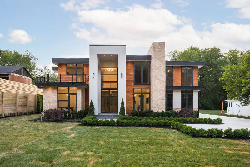 Modern custom home with a two-story glass entry, cedar siding, stone chimney and manicured front lawn