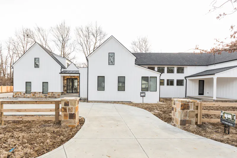 White board-and-batten modern farmhouse with stone accents, black windows and a curved concrete drive