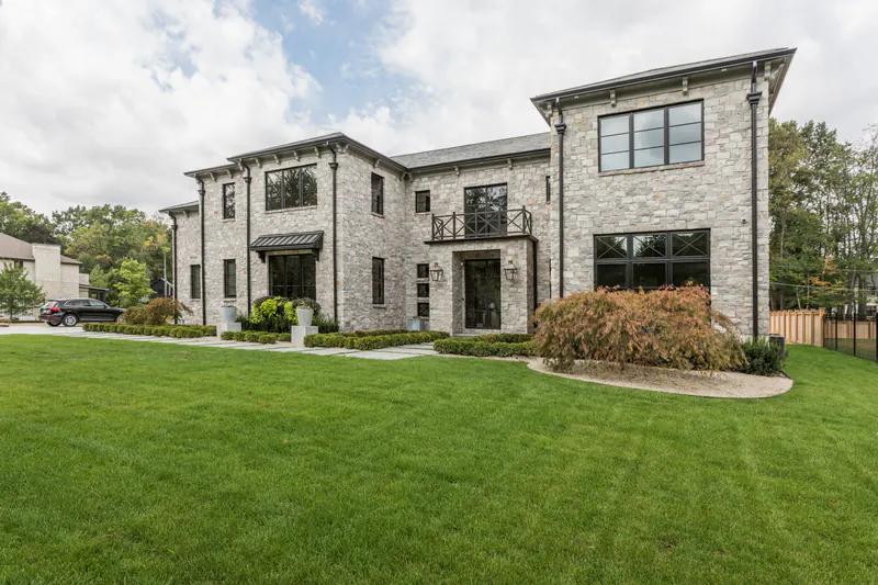 Two-story stone custom estate home with black steel windows and a wrought-iron Juliet balcony