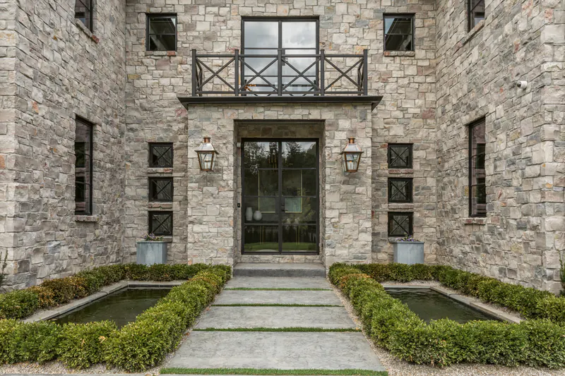 Stone estate home entry with steel-framed glass doors, lanterns and twin reflecting pools edged in boxwood