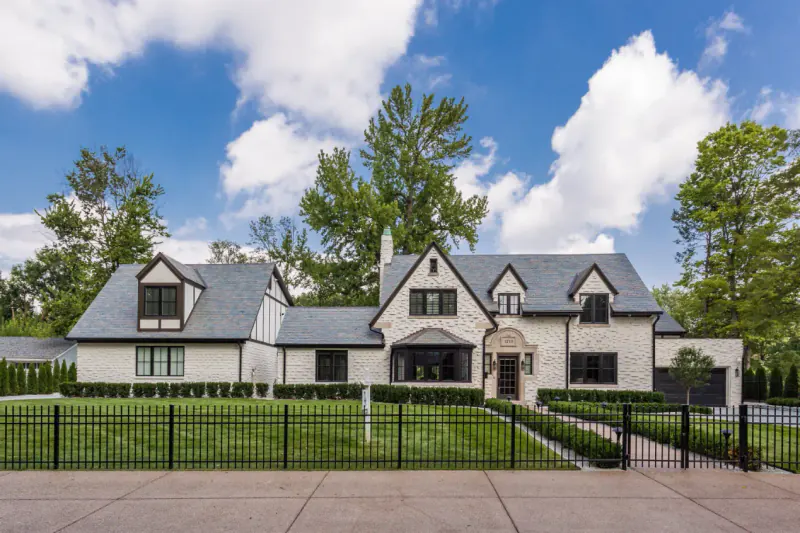 Tudor-inspired white brick home with a gray slate roof, half-timbered gable and black iron fence