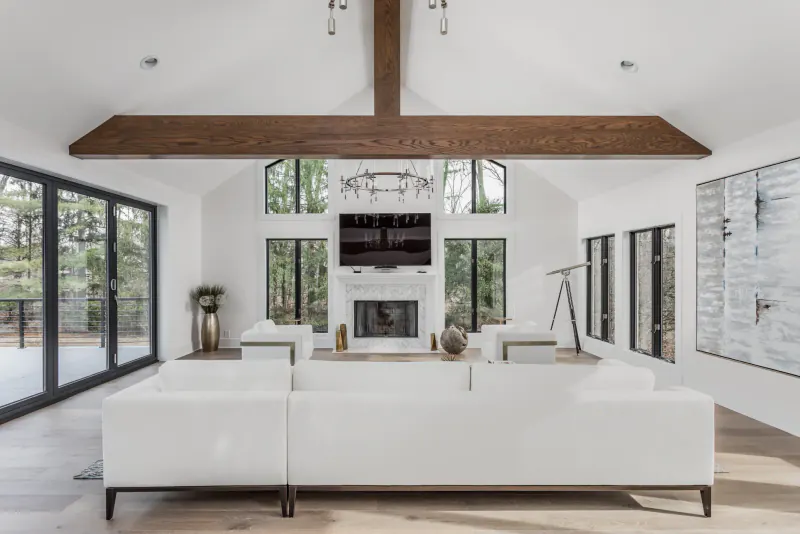 Bright vaulted living room with a stained wood ceiling beam, marble fireplace and white sectional sofa