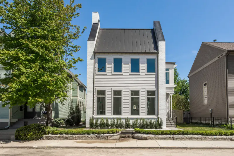 Narrow white home with brick end chimneys and a standing-seam metal roof on a tree-lined street